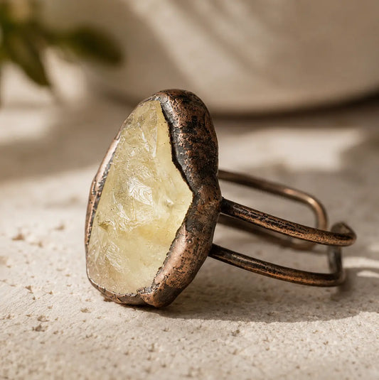 Yellow gemstone ring displayed on pale stone with soft greenery and warm natural styling.