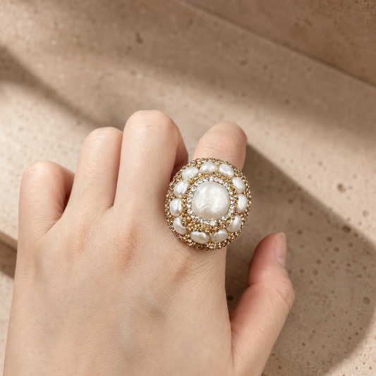 Baroque pearl ring with natural pearl center, gold-tone setting, and soft sunlight on a neutral stone background.