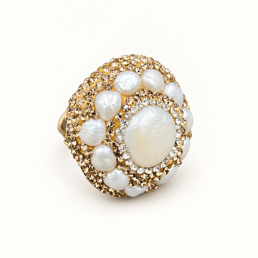 Gold-tone baroque pearl ring with an oval face, smaller surrounding pearls and clear accents on an off-white background.