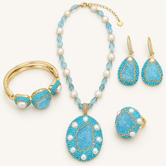 Aquamarine jewelry set with a beaded necklace, freshwater pearls, drop earrings, a bangle and a ring on an off-white background.