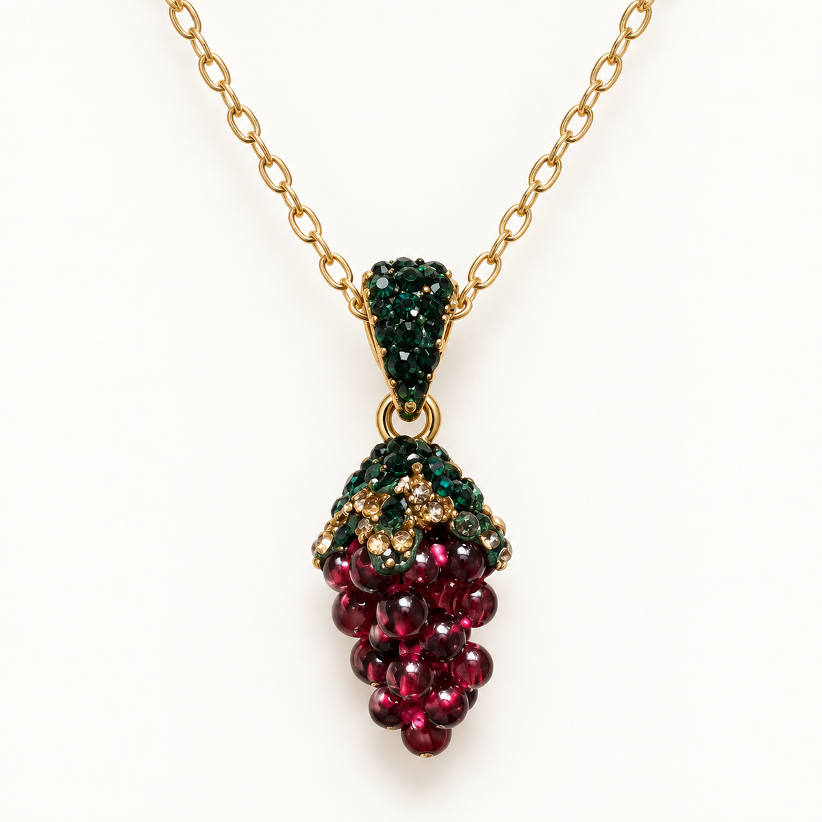Gold-tone pendant necklace with a burgundy grape cluster and green accents on a plain off-white background.