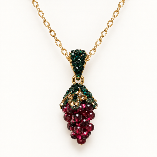 Garnet pendant necklace with a wine-red grape cluster, green crystal accents and a gold-tone chain on an off-white background.