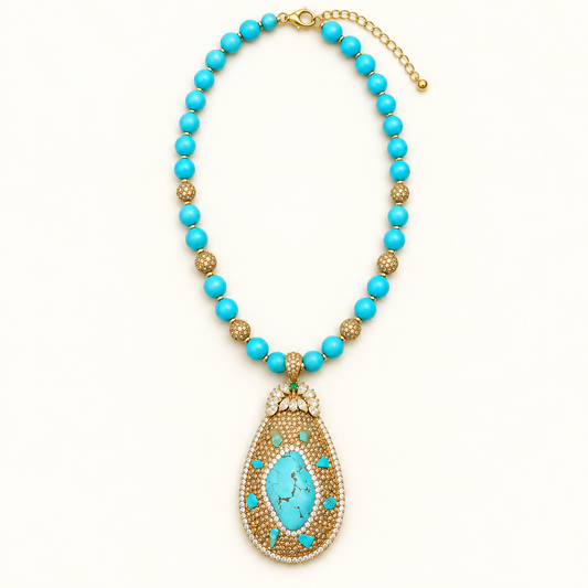 Turquoise beaded necklace with a gold-tone teardrop pendant and fastened clasp on an off-white background.