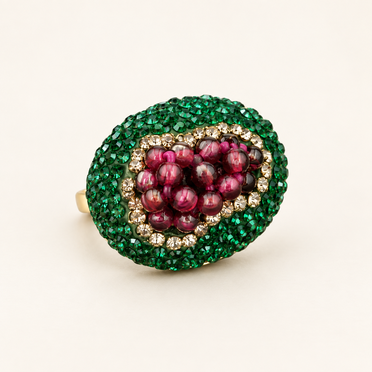 Garnet statement ring with wine-red grape-cluster beads and a green oval crystal border, tilted on an off-white background.