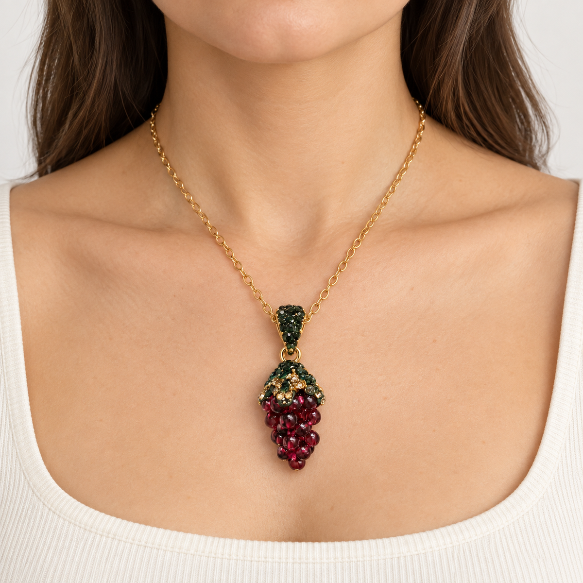 Front view of a woman wearing a grape-cluster pendant necklace with a gold-tone chain above an off-white neckline.