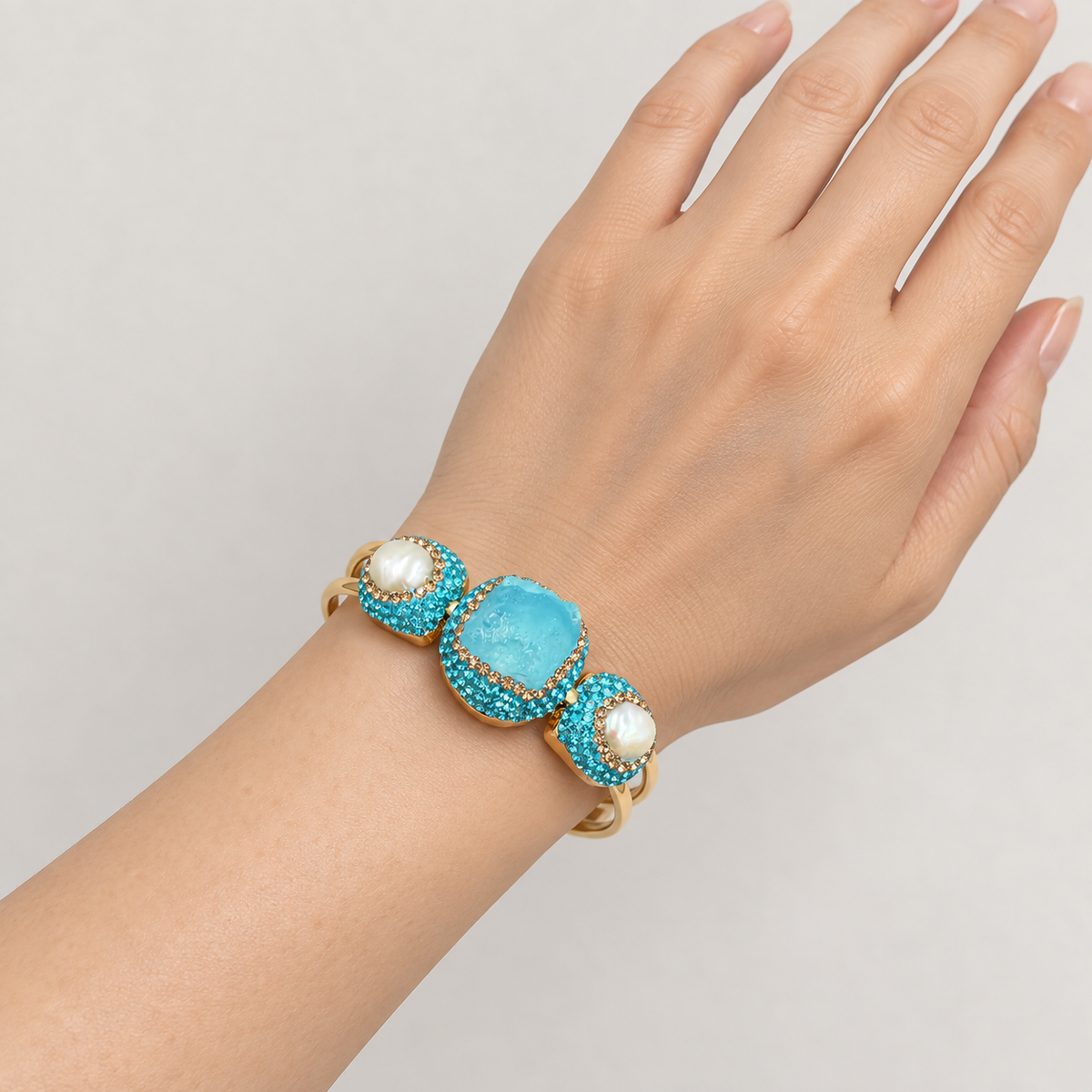 Turquoise bangle worn on the wrist, showing its decorative front, freshwater pearls and twin gold-tone bands.