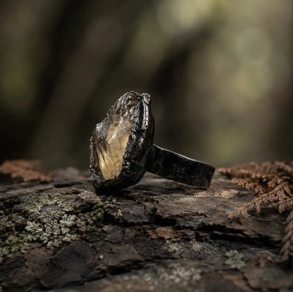 Yellow gemstone ring displayed on mossy wood with warm crystal glow and earthy natural mood.