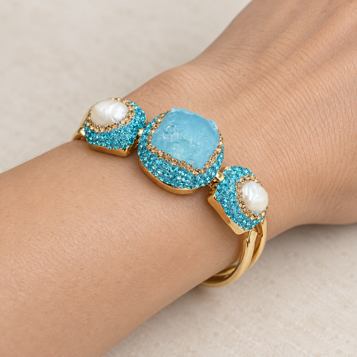 Close-up of a turquoise bracelet on the wrist, showing the textured raw stone, freshwater pearls and blue Czech crystal borders.