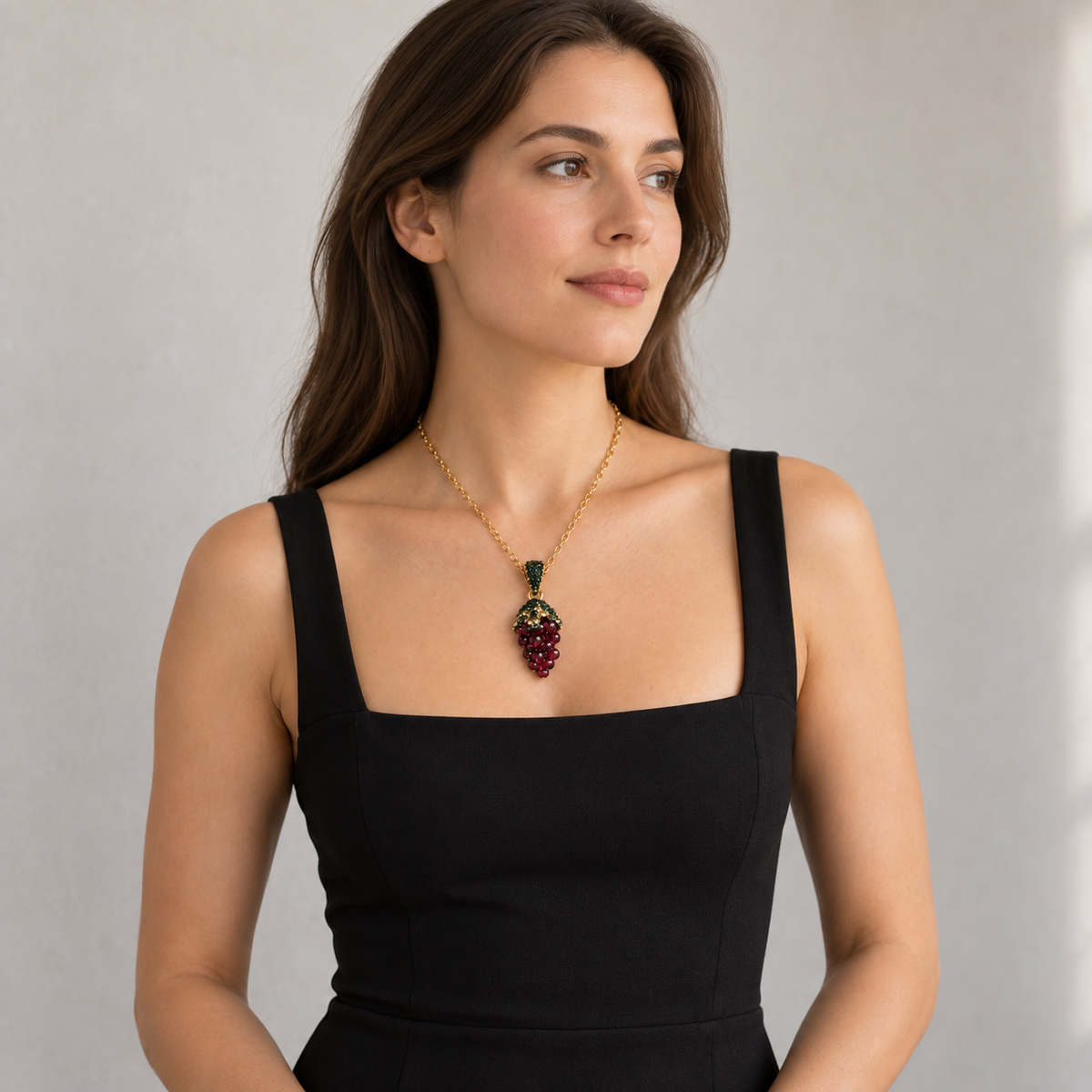 Woman in a black square-neck outfit wearing a burgundy grape-cluster pendant necklace, shown from the waist up.