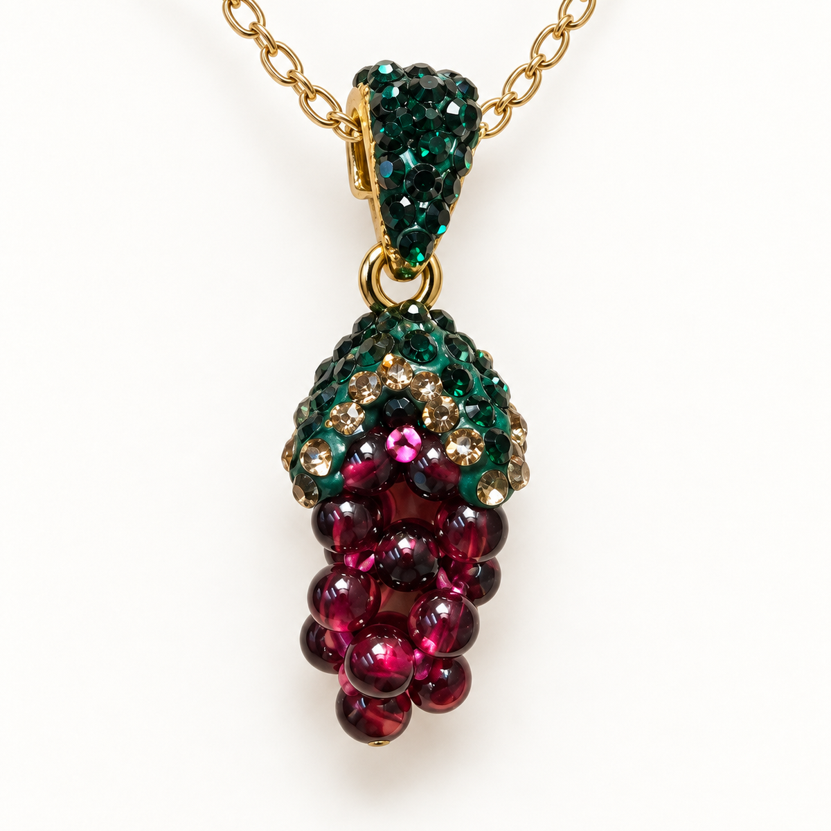 Macro view of a grape-cluster pendant necklace showing burgundy beads, green accents and a gold-tone connecting ring.