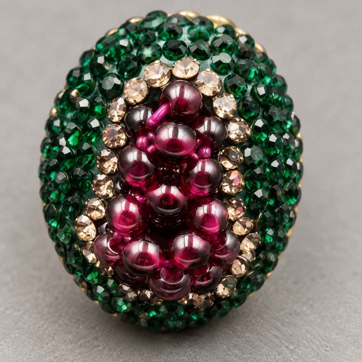 Macro view of the garnet grape-cluster ring showing polished wine-red beads, champagne crystals and a faceted green outer border.