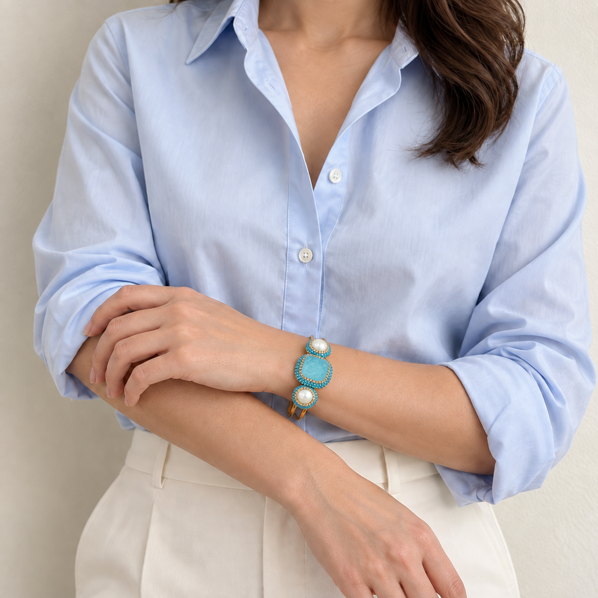 Turquoise bracelet with freshwater pearl accents worn with a pale blue shirt and ivory trousers.
