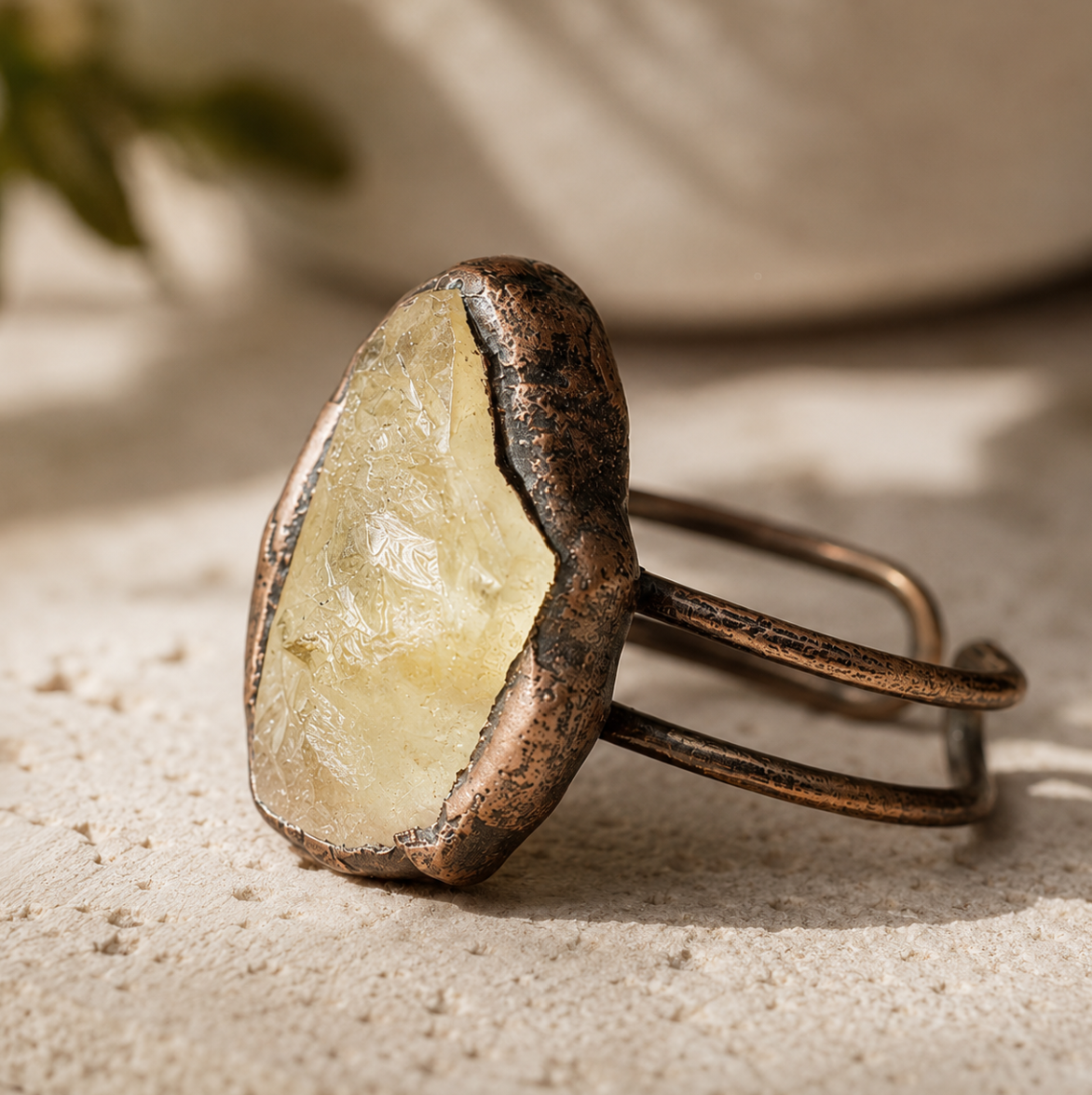Yellow gemstone ring displayed on pale stone with soft greenery and warm natural styling.