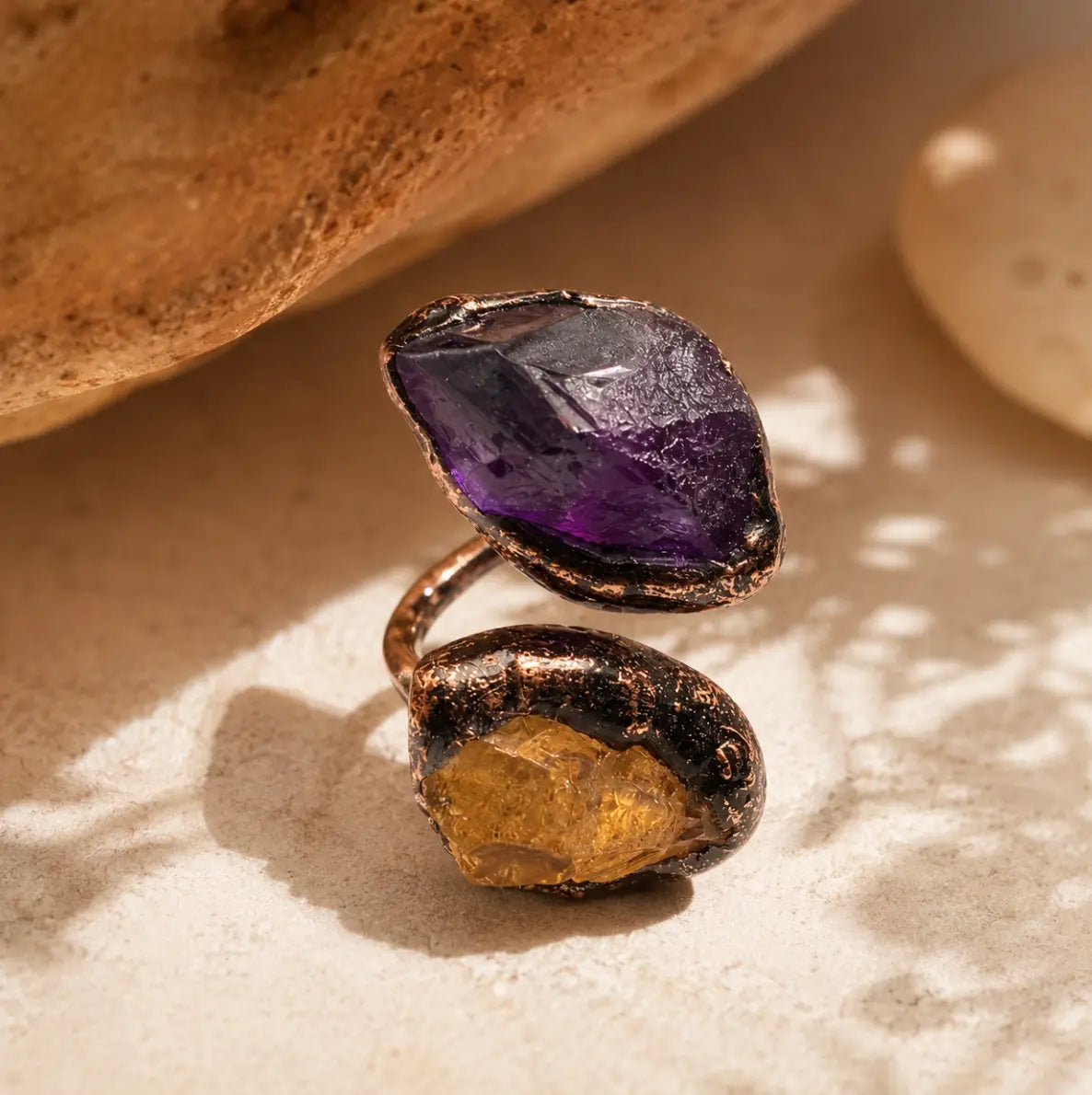 Purple yellow gemstone ring displayed on warm stone with bold two-stone contrast and artistic styling.