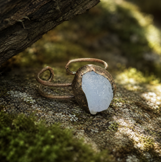Blue gemstone ring displayed on mossy stone with ocean-inspired color and earthy styling.