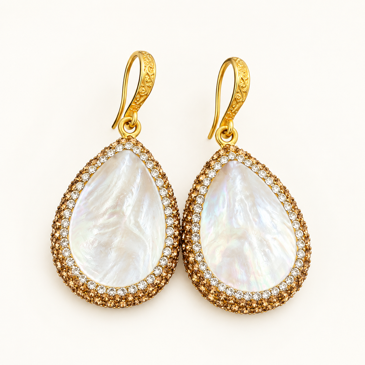 Gold mother of pearl earrings with white teardrop shell centers and sparkling borders on an off-white background