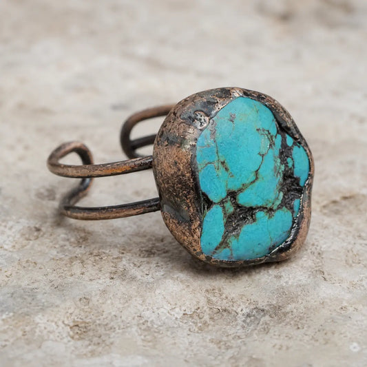 Natural turquoise ring displayed on pale stone with soft greenery and an earthy refined mood.
