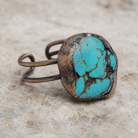 Natural turquoise ring displayed on pale stone with soft greenery and an earthy refined mood.