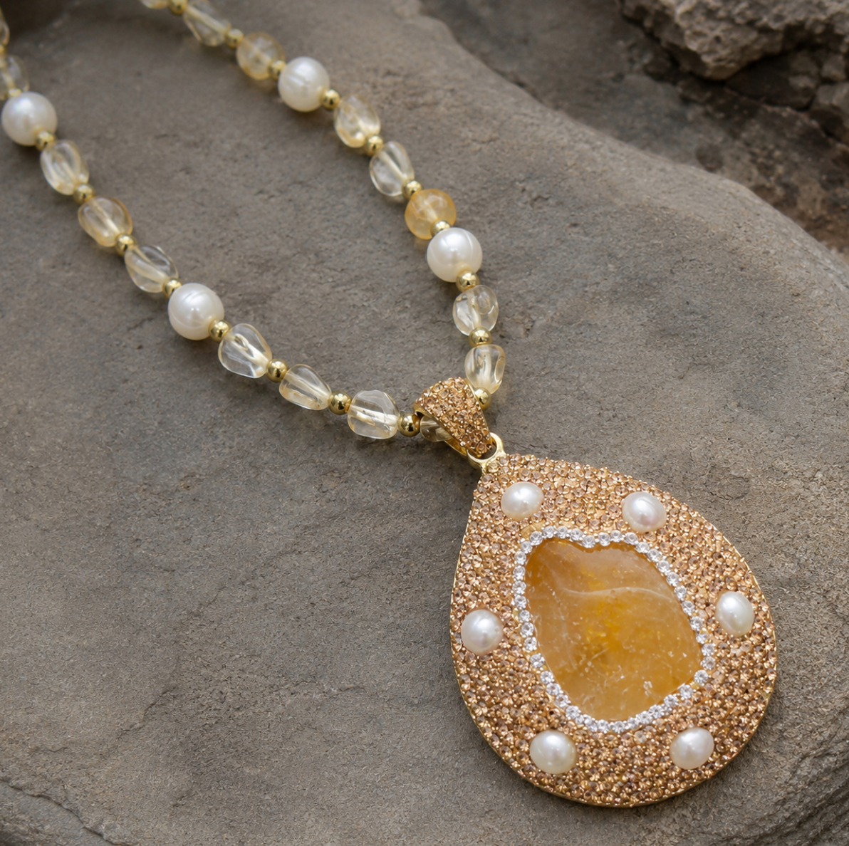 Citrine necklace with golden crystal pendant, pearl beads, and soft sunlight on a natural stone background.