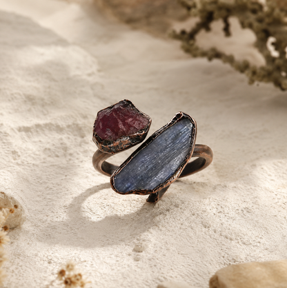 Red gemstone ring with raw red stone, elongated blue crystal, and sculptural vintage metal setting.