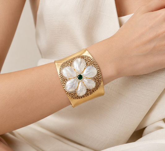 Wide gold-tone mother-of-pearl bracelet worn on the wrist, showing white flower petals and a deep green center.