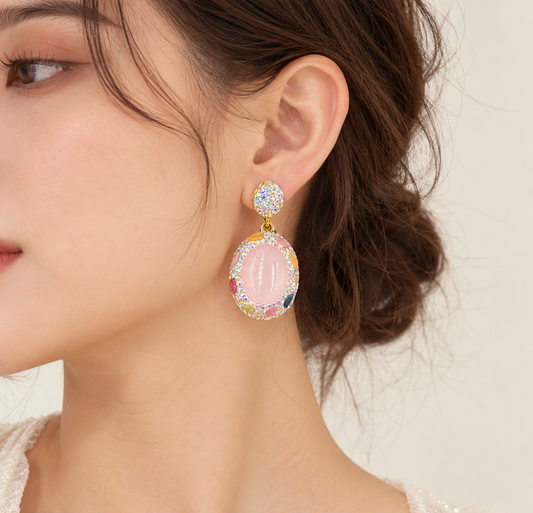 Close-up of a rose quartz earring worn at the ear, with an oval pink stone hanging from a sparkling round stud.
