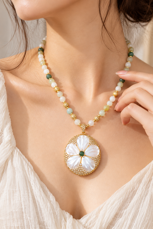 Close-up of a mother-of-pearl flower necklace worn with a white V-neck top, showing the floral pendant and freshwater pearl strand.