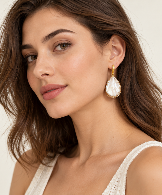 Woman wearing mother-of-pearl teardrop earrings with gold-tone details, shown beside the face.