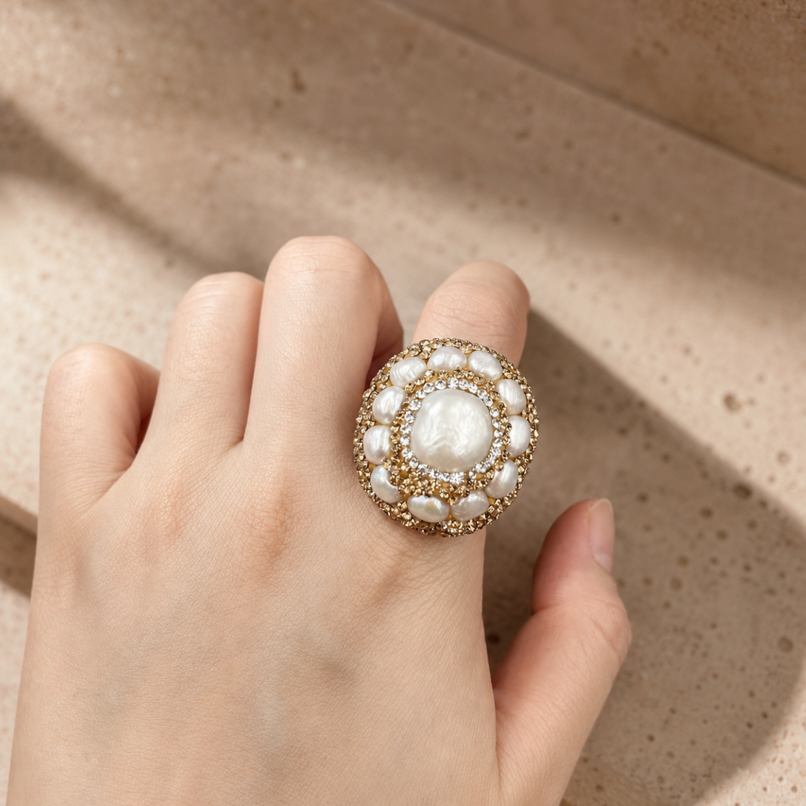 Baroque pearl ring with natural pearl center, gold-tone setting, and soft sunlight on a neutral stone background.