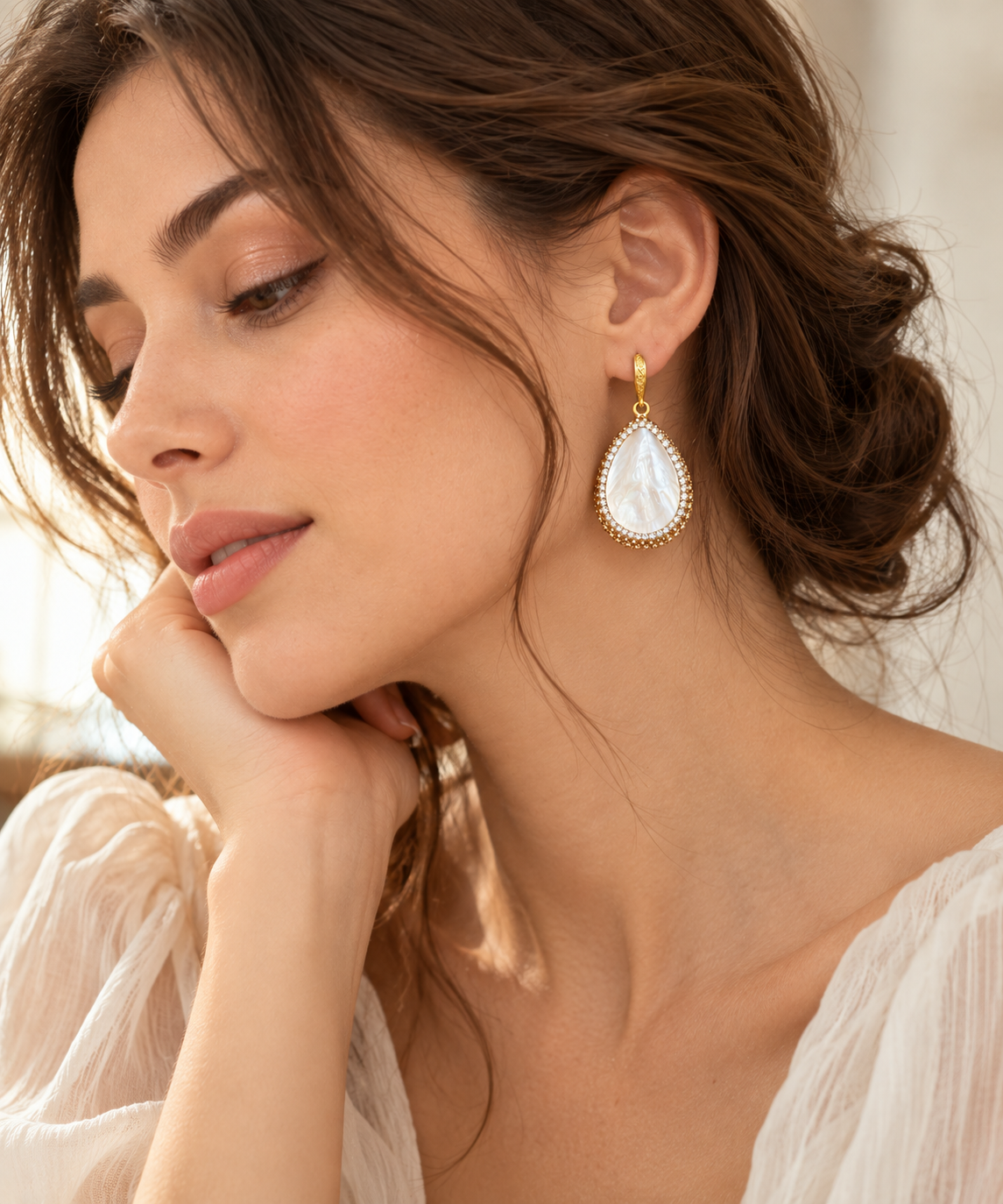 Close-up of gold shell earrings with white mother of pearl teardrops worn below the ear
