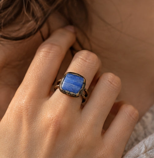 Blue stone ring worn on a woman's finger, showing the scale of the deep blue crystal and double-band design.