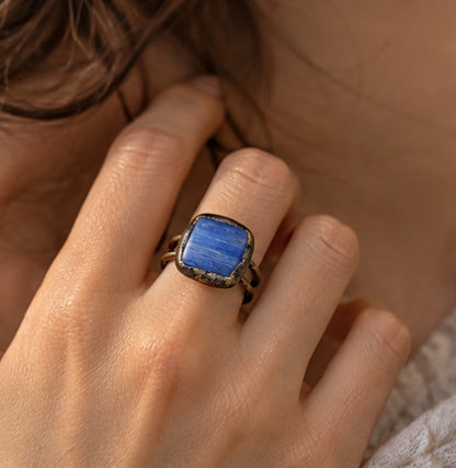 Blue stone ring worn on a woman's finger, showing the scale of the deep blue crystal and double-band design.
