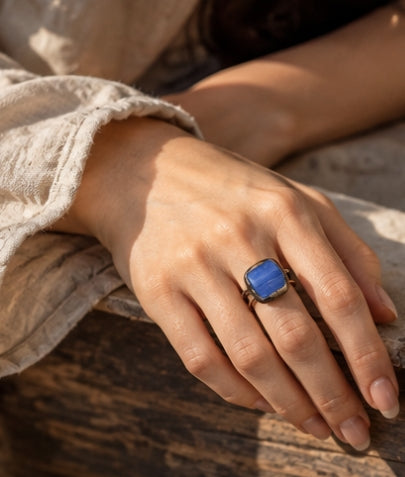 Close-up of a blue stone ring worn on the hand, highlighting the square crystal, dark setting, and double band.