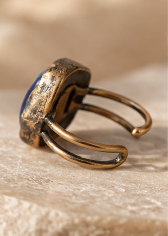 Macro view of the blue stone ring showing the crystal's striated surface, rounded square shape, and dark setting.