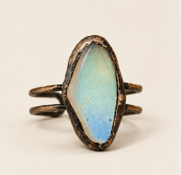 Blue stone ring with an elongated oval moonstone, dark-toned setting and split open band on warm off-white