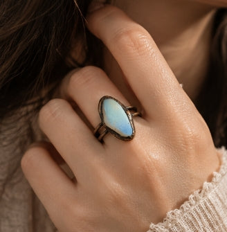 Moonstone blue stone ring worn on the hand, showing its elongated oval scale against a soft cream blouse