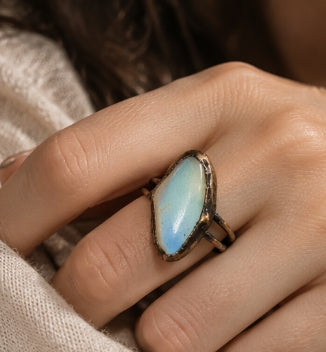 Statement cocktail ring worn beside the face, with pale blue-green moonstone and cream textured clothing