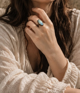 Blue moonstone ring worn with a relaxed cream outfit, showing the elongated oval stone in natural light
