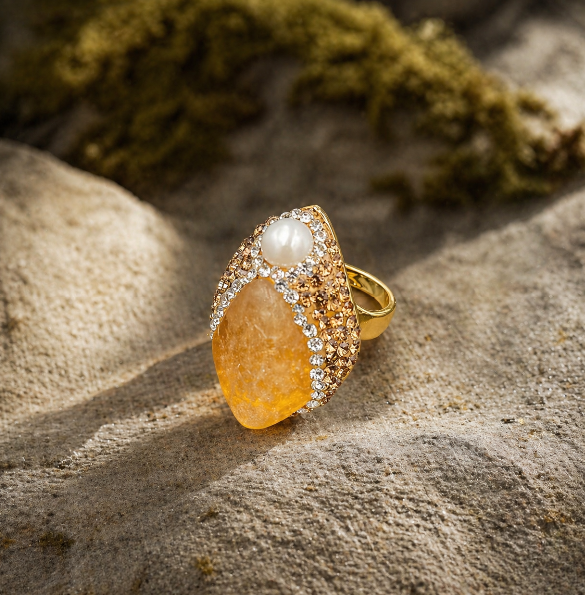 Citrine ring with golden yellow crystal, pearl accent, and warm sunlight on a natural stone background.