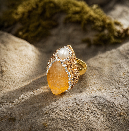 Citrine ring with golden yellow crystal, pearl accent, and warm sunlight on a natural stone background.