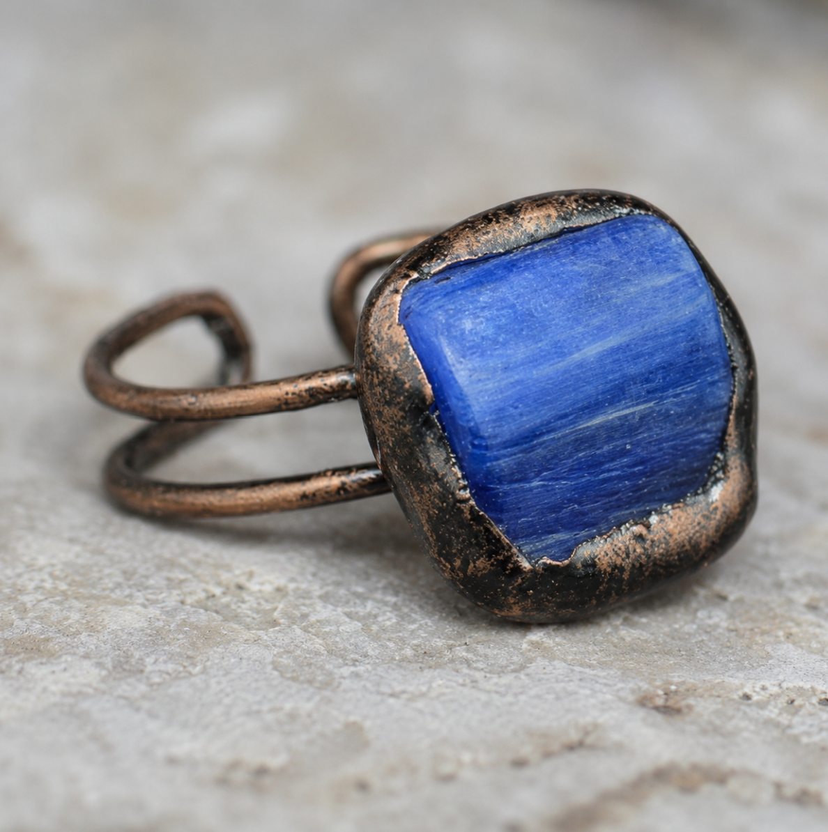 Blue crystal ring with deep rectangular stone, sculptural setting, and refined modern styling.