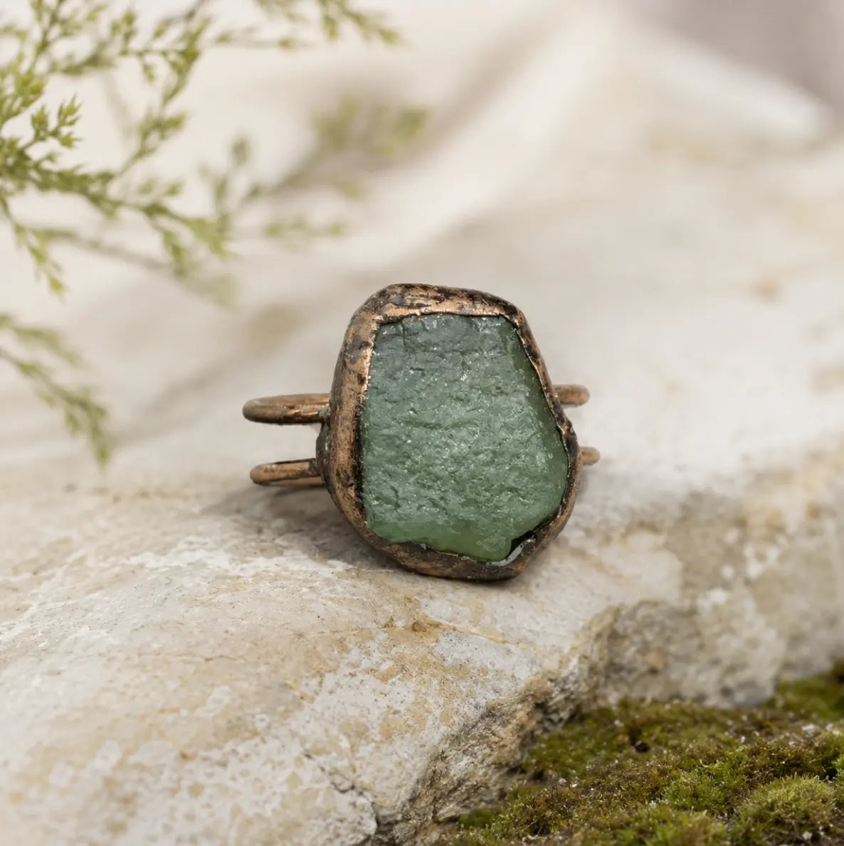 Green crystal ring with raw stone texture, muted forest color, and handcrafted-looking form.