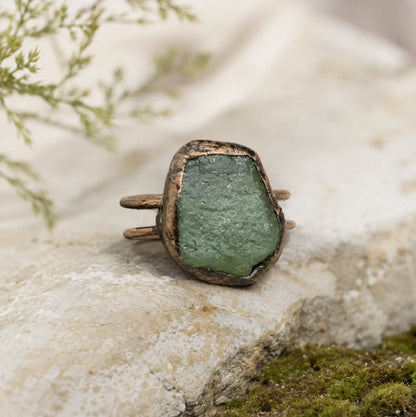 Green crystal ring with raw stone texture, muted forest color, and handcrafted-looking form.