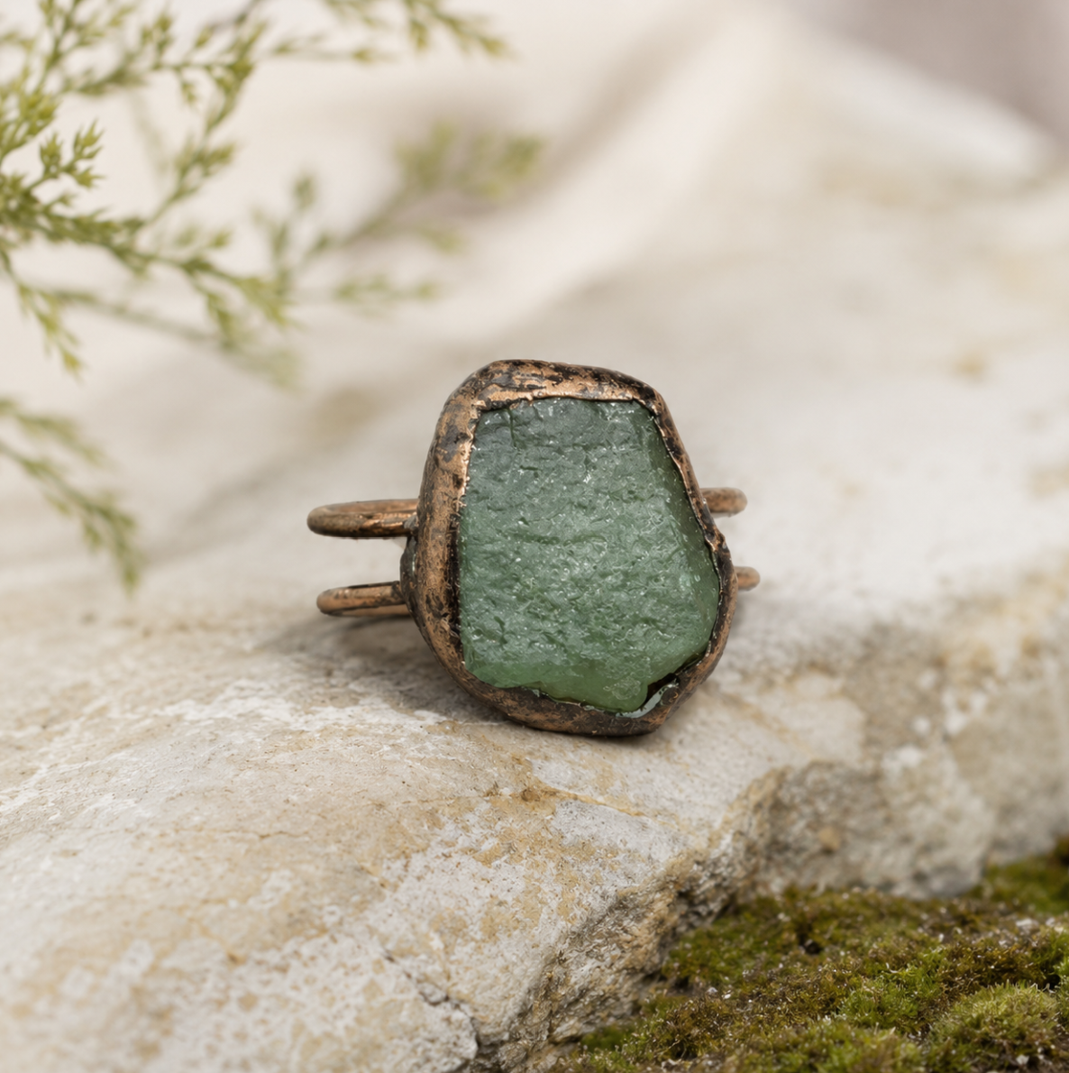 Green crystal ring with raw stone texture, muted forest color, and handcrafted-looking form.