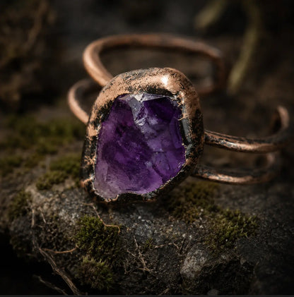 Amethyst crystal ring displayed on mossy stone with natural texture and soft shadowed light.