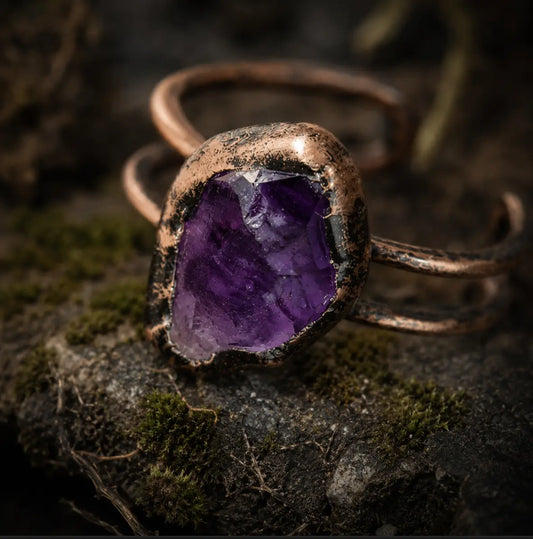 Amethyst crystal ring displayed on mossy stone with natural texture and soft shadowed light.