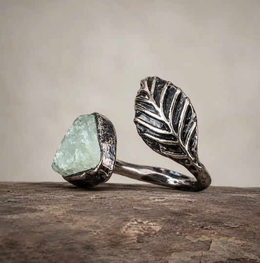 Green fluorite feather ring with pale green crystal, sculpted silver-tone feather, and rustic natural setting.