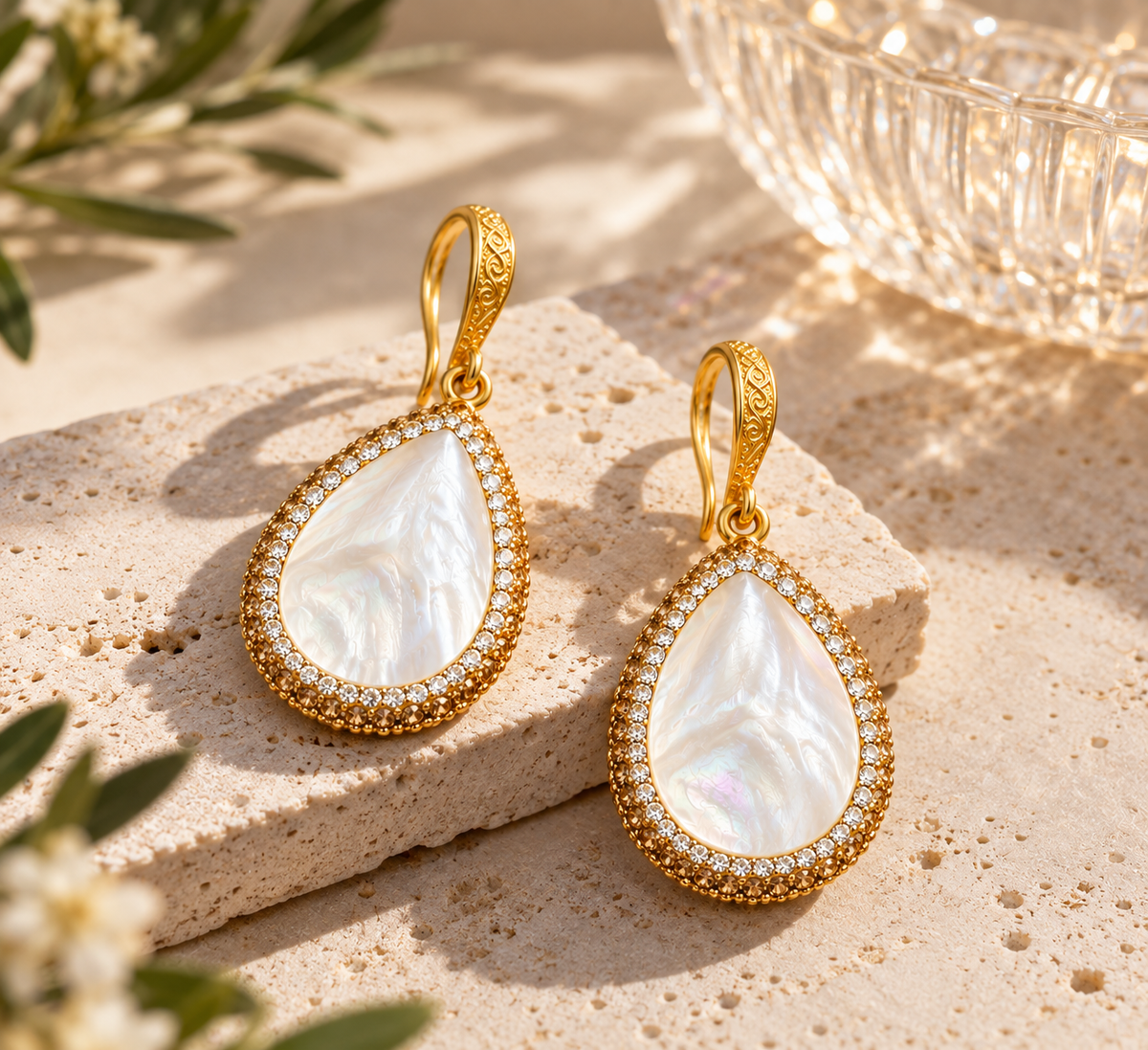 Gold seashell earrings with luminous white mother of pearl teardrops styled on warm natural stone