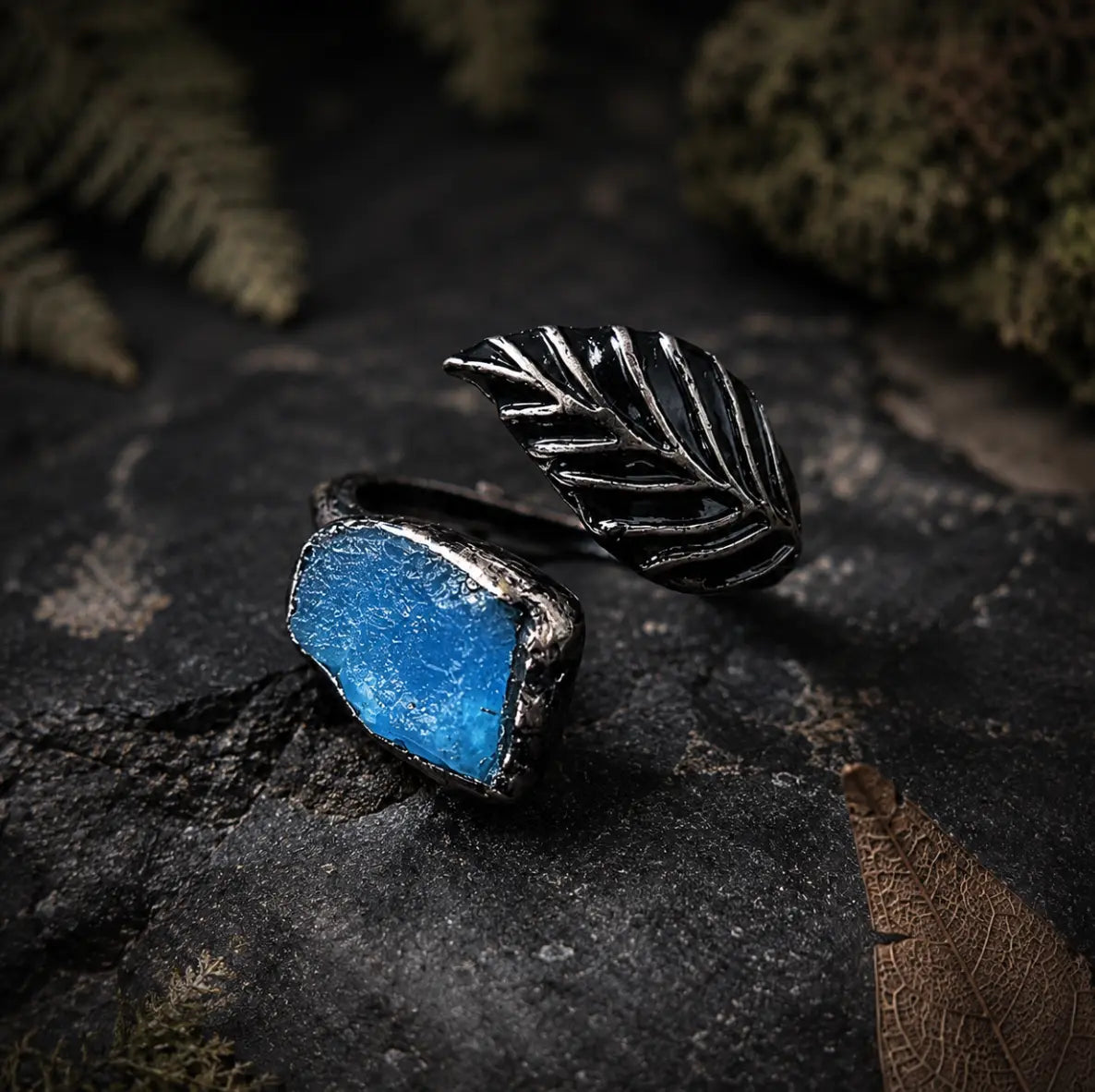 Apatite feather ring displayed on wood and stone with moss, soft shadows, and woodland styling.