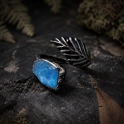 Apatite feather ring displayed on wood and stone with moss, soft shadows, and woodland styling.